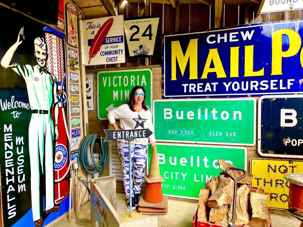 Woman standing in front of vintage road signs in Mendenhall's Museum in Buellton, CA.